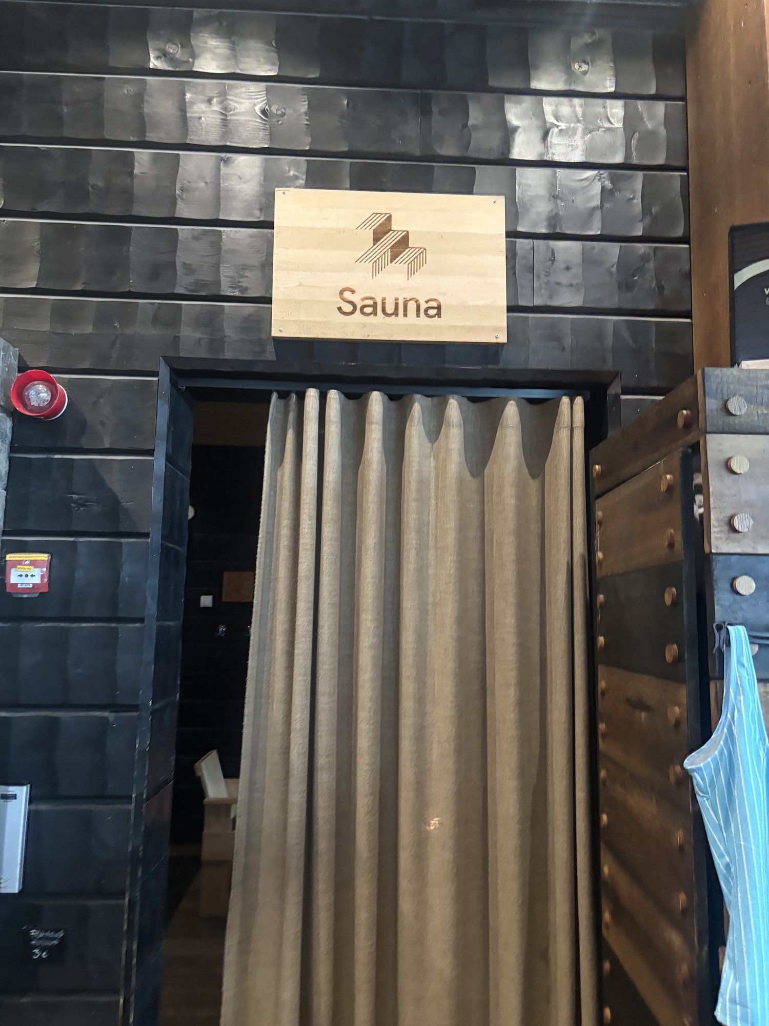 木製の扉に取り付けられた「Sauna」の看板と、入口の布製カーテン
