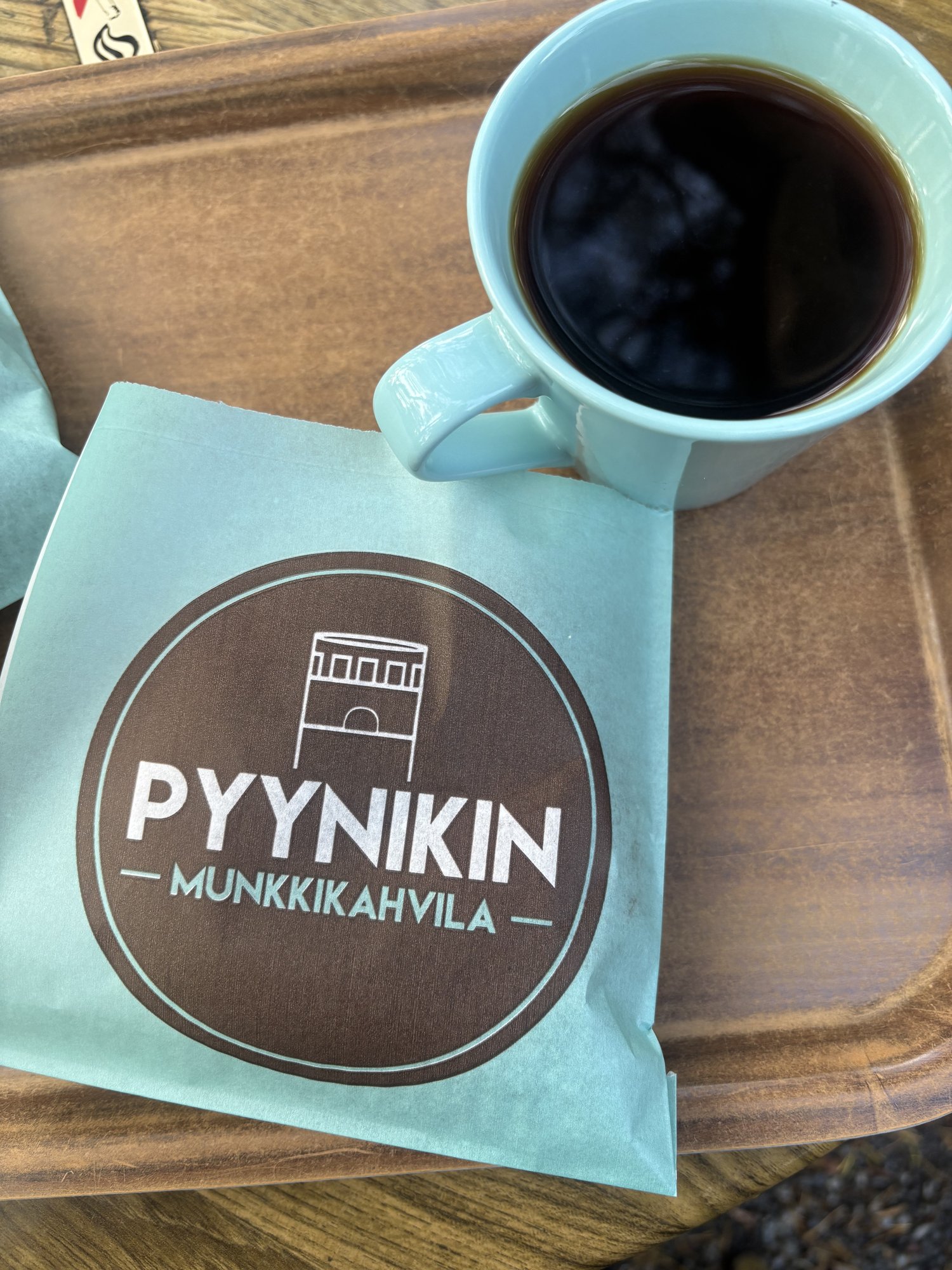 「PYYNIKIN MUNKKIKAHVILA」のロゴが入った紙袋と、水色のカップに入ったコーヒー